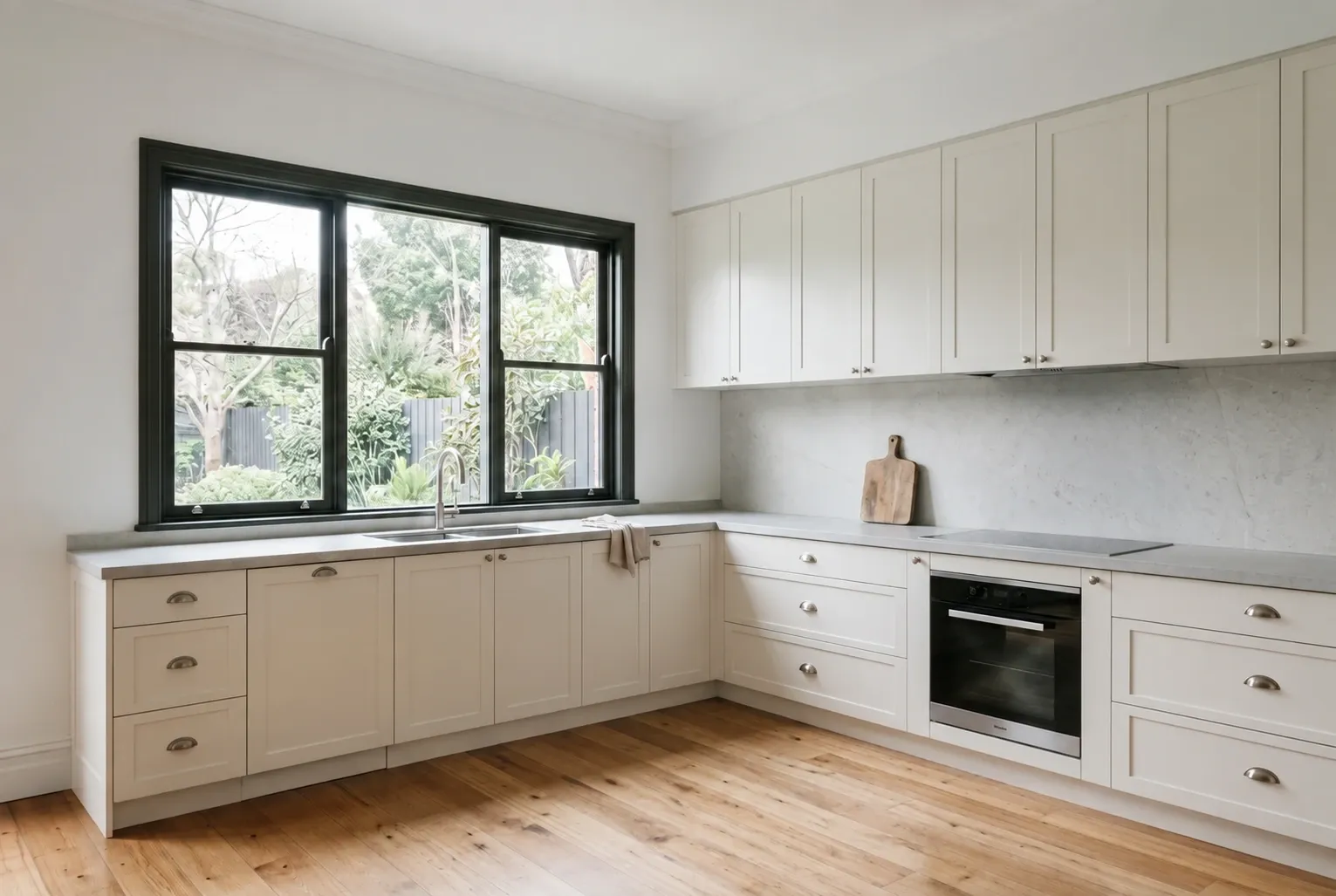 Kitchen inspiration with warm off-white Shaker cabinetry, a window-side sink and clear L-shaped benchtop