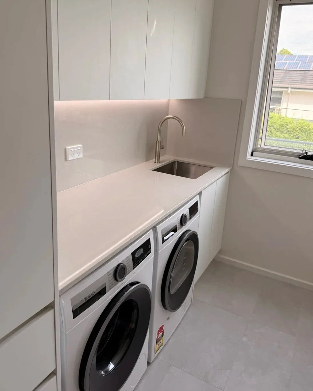 compact white laundry with overhead cabinetry and stone bench