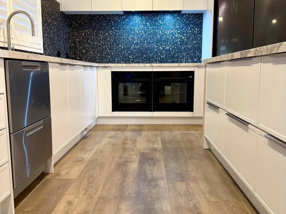 Completed Bluestone kitchen with white cabinetry, dark mosaic splashback and timber-look flooring