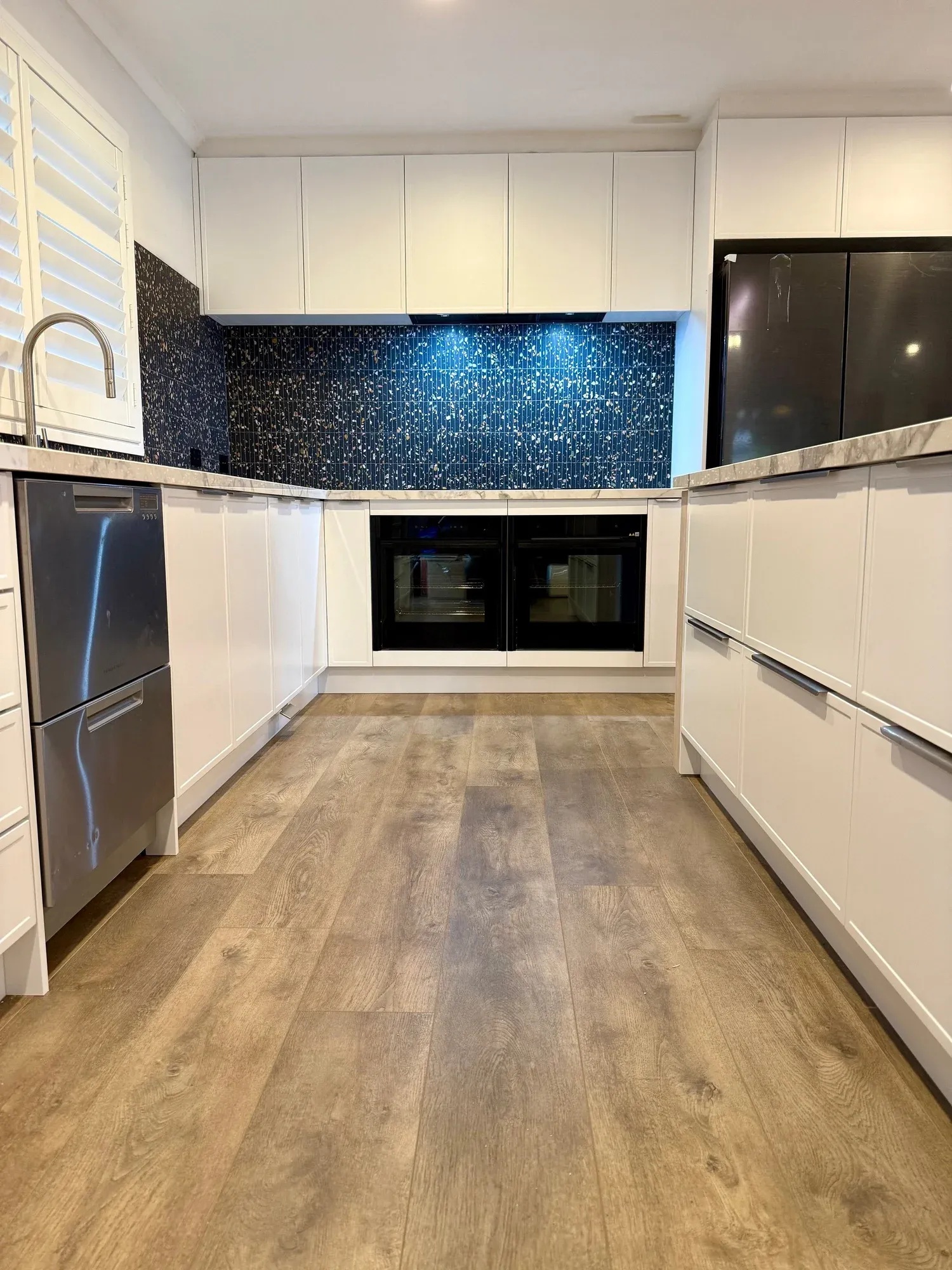 Full-height view of a completed Bluestone kitchen with white cabinetry, dark mosaic splashback and timber-look flooring