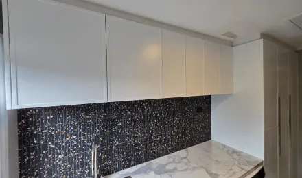 White overhead laundry cupboards above the mosaic splashback and benchtop