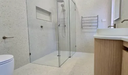 Glass shower with a tiled niche beside the curved timber vanity in the completed bathroom