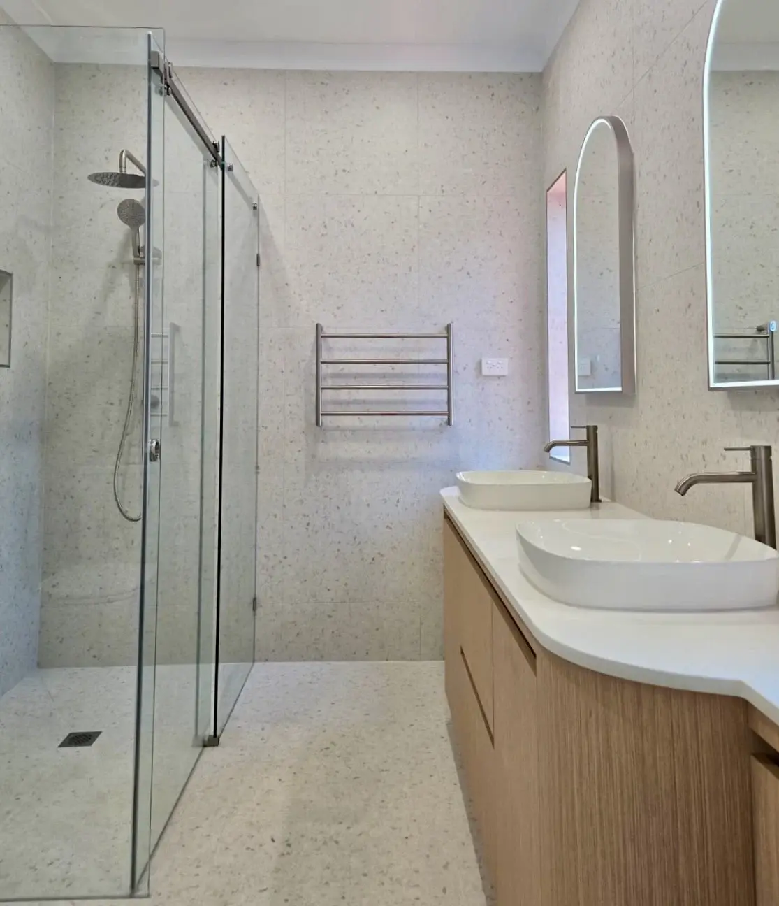 Completed Bluestone bathroom with a curved timber vanity, twin basins and arched mirrors