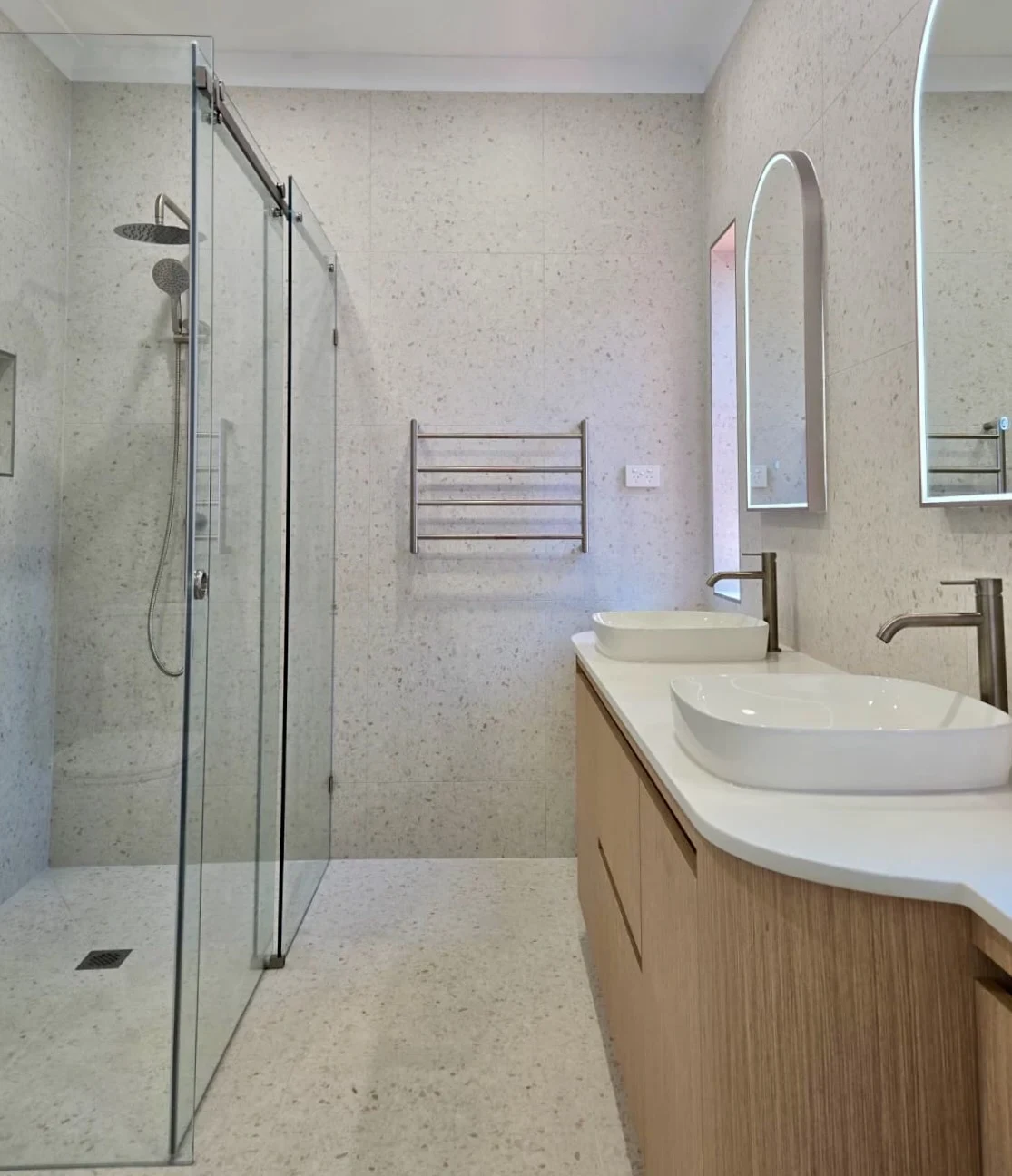 A completed Bluestone bathroom with a curved timber vanity, twin basins and arched mirrors.