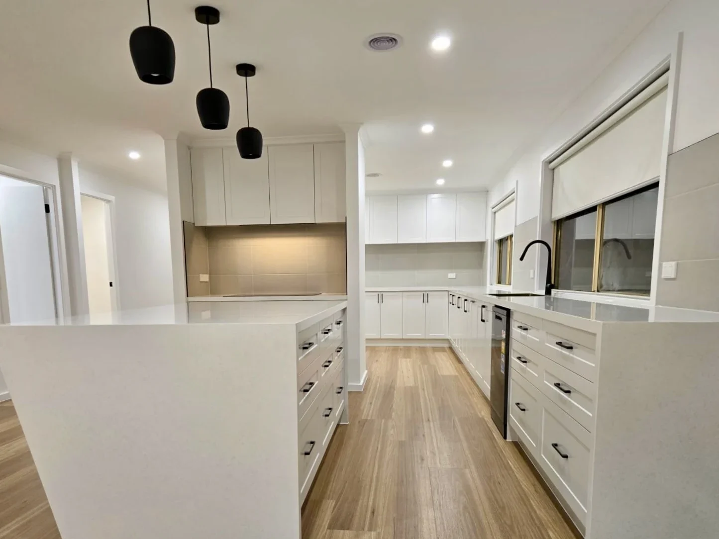 Completed white kitchen with black pendant lights, island drawers and timber flooring